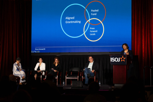 Woman at podium on stage and four people in chairs
