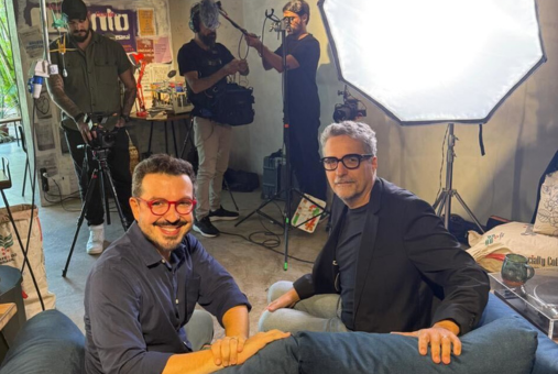 Journalist Guilherme Amado (left) and filmmaker Kleber Mendonça Filho (right) on set, surrounded by lighting equipment and a film crew, during the recording of a warm-up episode for Papo Amado, a YouTube interview show set to launch in June.